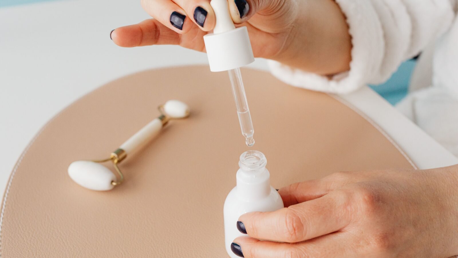 a woman using a facial tapping tool with a serum bottle on a marble countertop