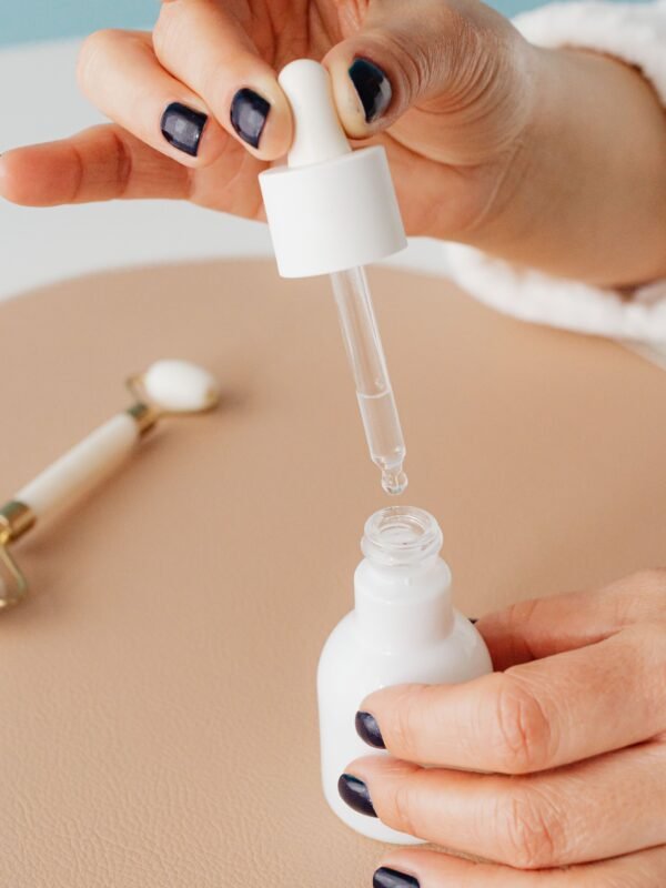 a woman using a facial tapping tool with a serum bottle on a marble countertop